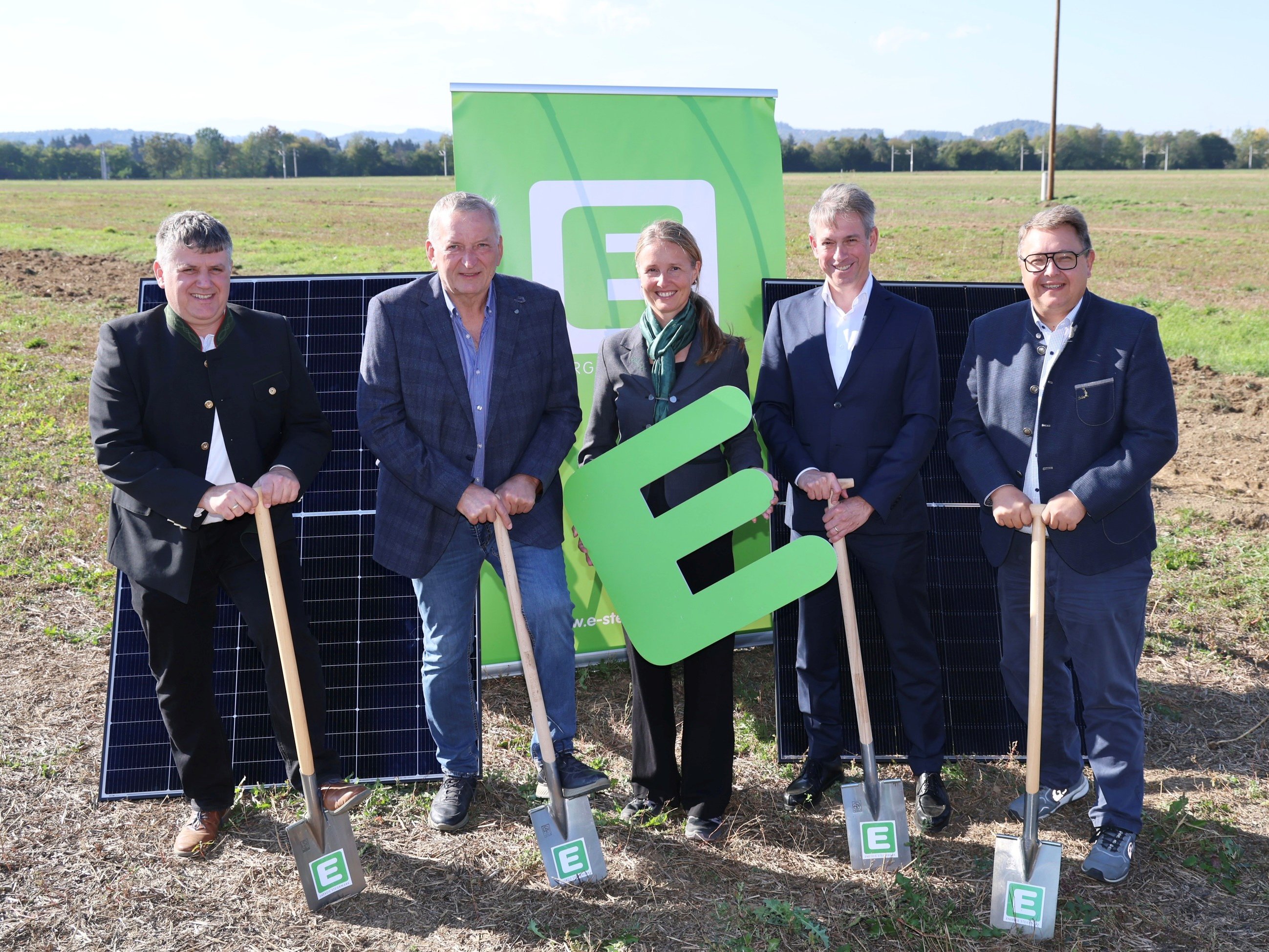 Fünf Personen mit Schaufeln und Solarmodulen vor einer grünen Tafel mit dem E-Logo in der Steiermark.